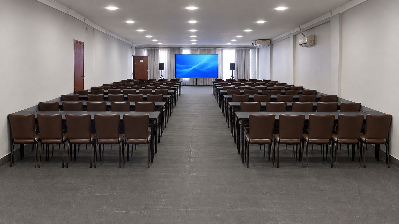 Auditório do Espaço Belladata no 2º piso, com mesas em formato escolar e cadeiras estofadas