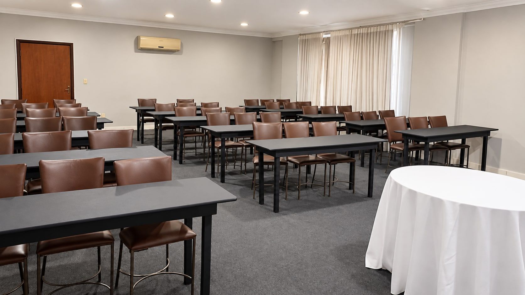Sala do 2º piso em formato escolar, com mesas retangulares, cadeiras estofadas marrons e uma mesa redonda com toalha branca